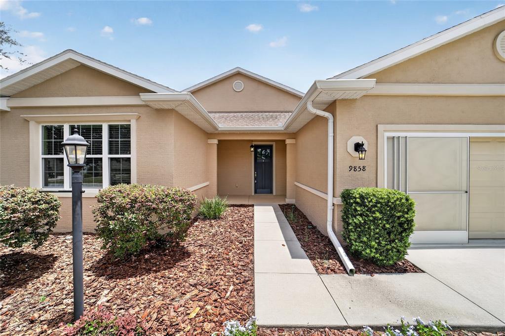A tan stucco house features a front walkway, a dark door, and a garage — 9858 SW 90TH STREET, OCALA, FL
