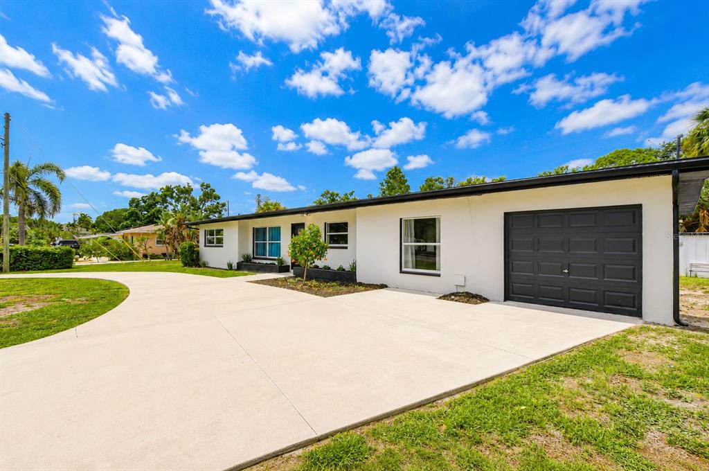 A white single-story house features a black garage door and a large concrete driveway — 6871 4TH STREET S, ST PETERSBURG, FL