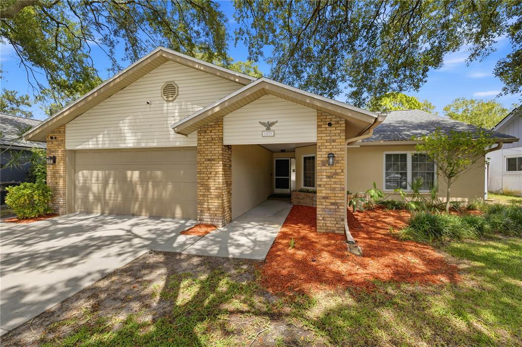 A single-story house with a beige stucco exterior, brick accents, and a two-car garage — 1570 CLUB DRIVE, TARPON SPRINGS, FL
