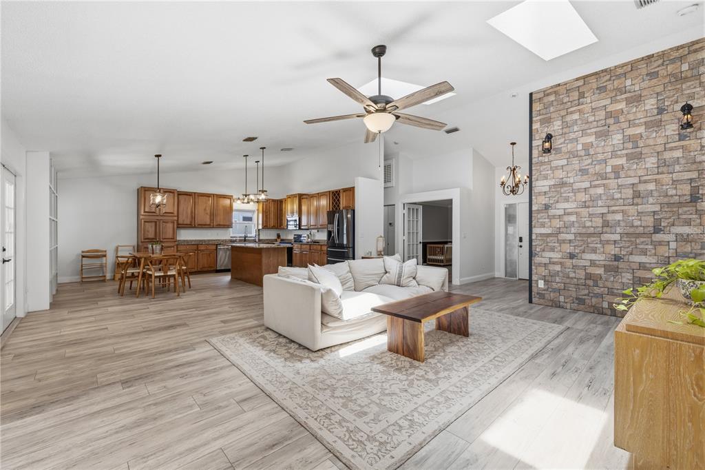 An open-concept living area features a stone accent wall, wood-look flooring, and a kitchen — 1570 CLUB DRIVE, TARPON SPRINGS, FL