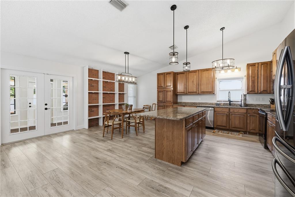 An open-concept kitchen and dining area features wood cabinets, a granite island, and brick shelving — 1570 CLUB DRIVE, TARPON SPRINGS, FL
