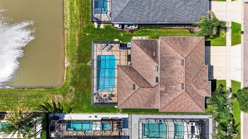 An aerial view shows a house with a screened-in pool and patio beside a lake — 7109 BAY LAUREL COURT, WESLEY CHAPEL, FL