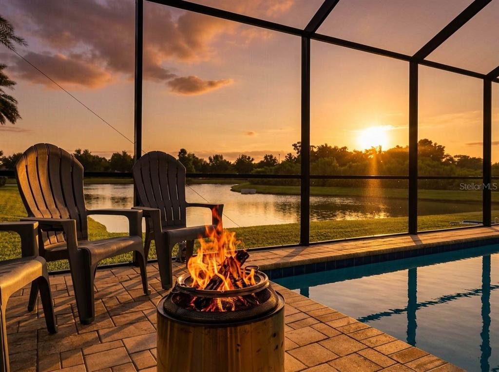A fire pit sits on a pool deck overlooking a lake at sunset — 7109 BAY LAUREL COURT, WESLEY CHAPEL, FL
