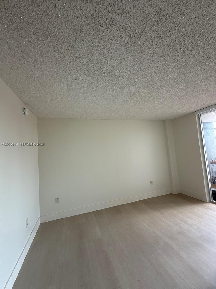 An empty room features light-colored wood-look flooring, plain white walls, and a textured popcorn ceiling — 1800 NW 24th Ave # 220, Miami FL 33125, MIAMI, FL