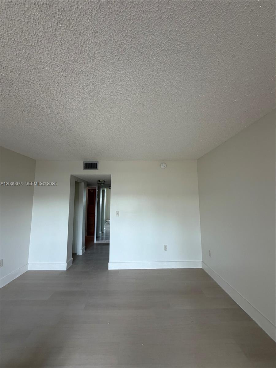 An empty room features light-colored wood-look flooring, white walls, and a textured popcorn ceiling — 1800 NW 24th Ave # 220, Miami FL 33125, MIAMI, FL