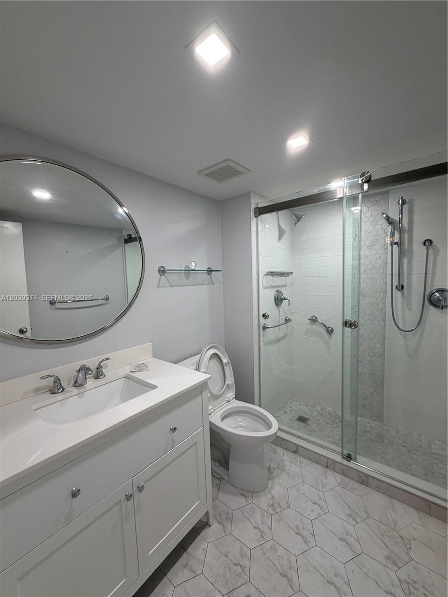 A bathroom features a white vanity, a round mirror, a toilet, and a glass shower — 1800 NW 24th Ave # 220, Miami FL 33125, MIAMI, FL