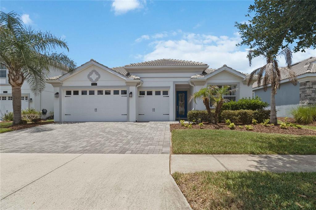 A single-story house with a paved driveway, a three-car garage, and a blue front door — 1361 OLYMPIC CLUB BOULEVARD, CHAMPIONS GATE, FL