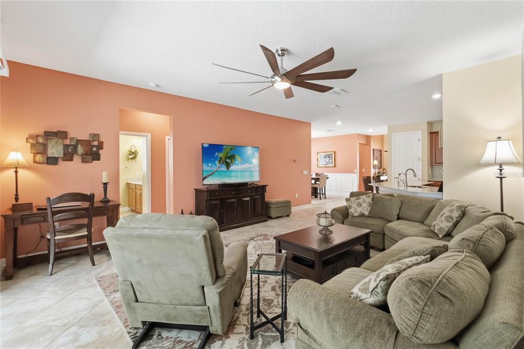 A living room features a coral wall, a sectional sofa, a recliner, and a ceiling fan — 1361 OLYMPIC CLUB BOULEVARD, CHAMPIONS GATE, FL