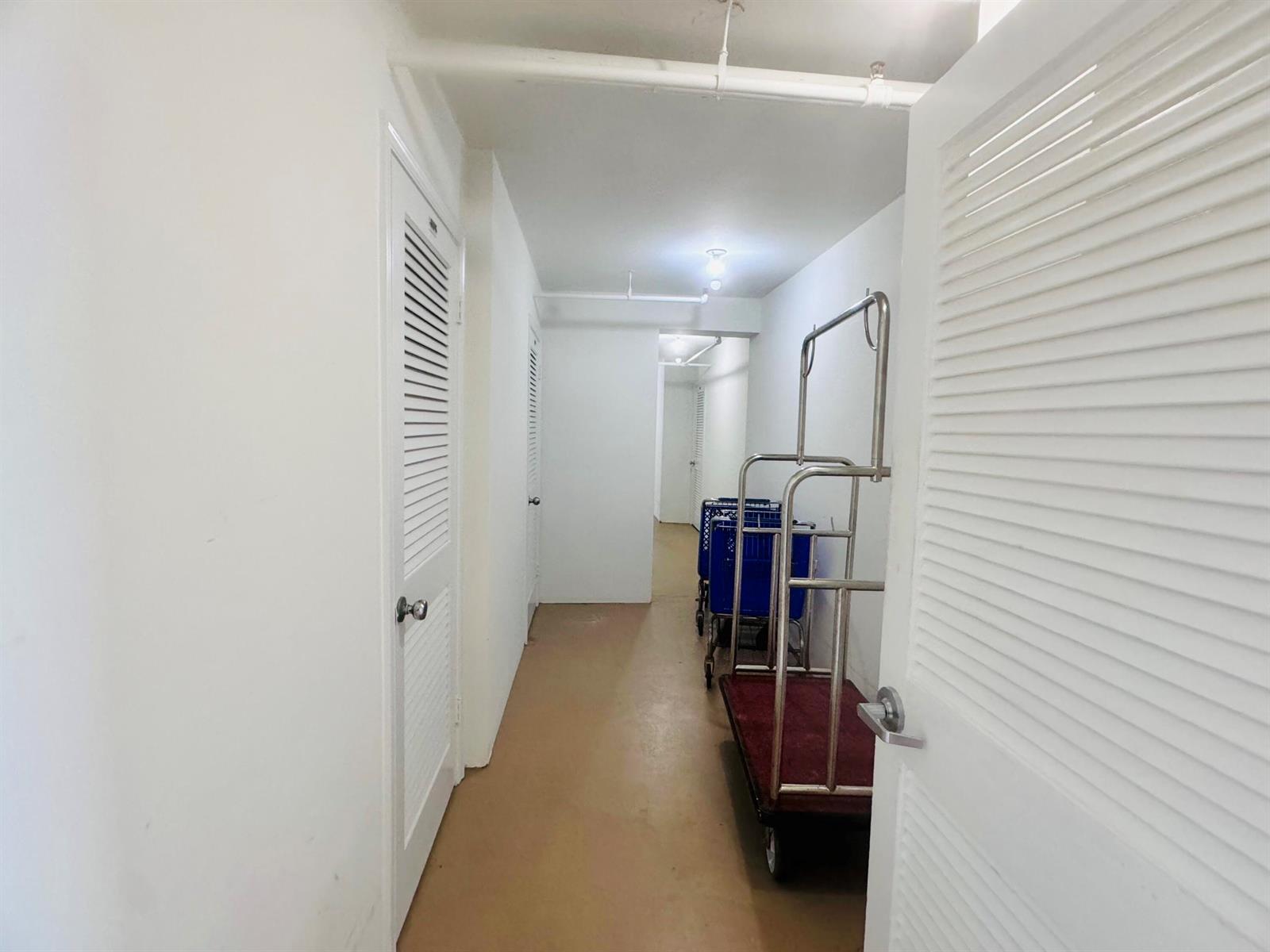 A narrow hallway with white walls, louvered doors, and a metal luggage cart — 200 S Beach Road # 403, Tequesta FL 33469, TEQUESTA, FL