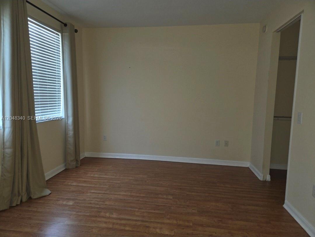 An empty bedroom features light-colored walls, wood-look flooring, a window with curtains, and a closet — 2900 NW 125th Ave # 319, Sunrise FL 33323, SUNRISE, FL