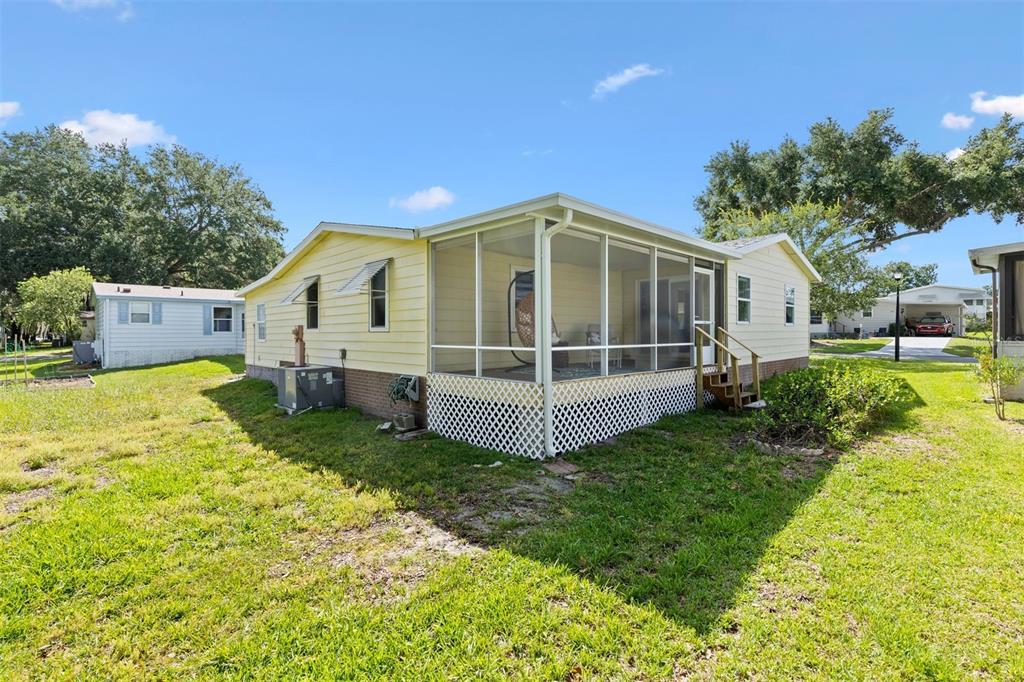 A yellow mobile home with a screened-in porch and lattice skirting sits on a lawn — 1726 HILTON HEAD BOULEVARD, LADY LAKE, FL