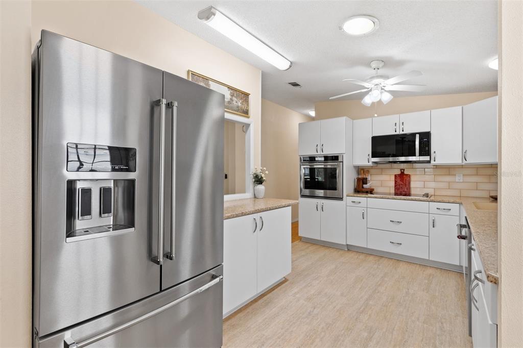 A kitchen features stainless steel appliances, white cabinetry, light countertops, and light-colored wood-look flooring — 1726 HILTON HEAD BOULEVARD, LADY LAKE, FL