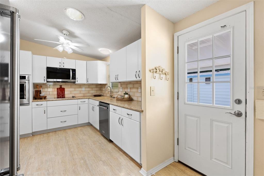A kitchen with white cabinets, light countertops, a stainless steel dishwasher, and a white door — 1726 HILTON HEAD BOULEVARD, LADY LAKE, FL
