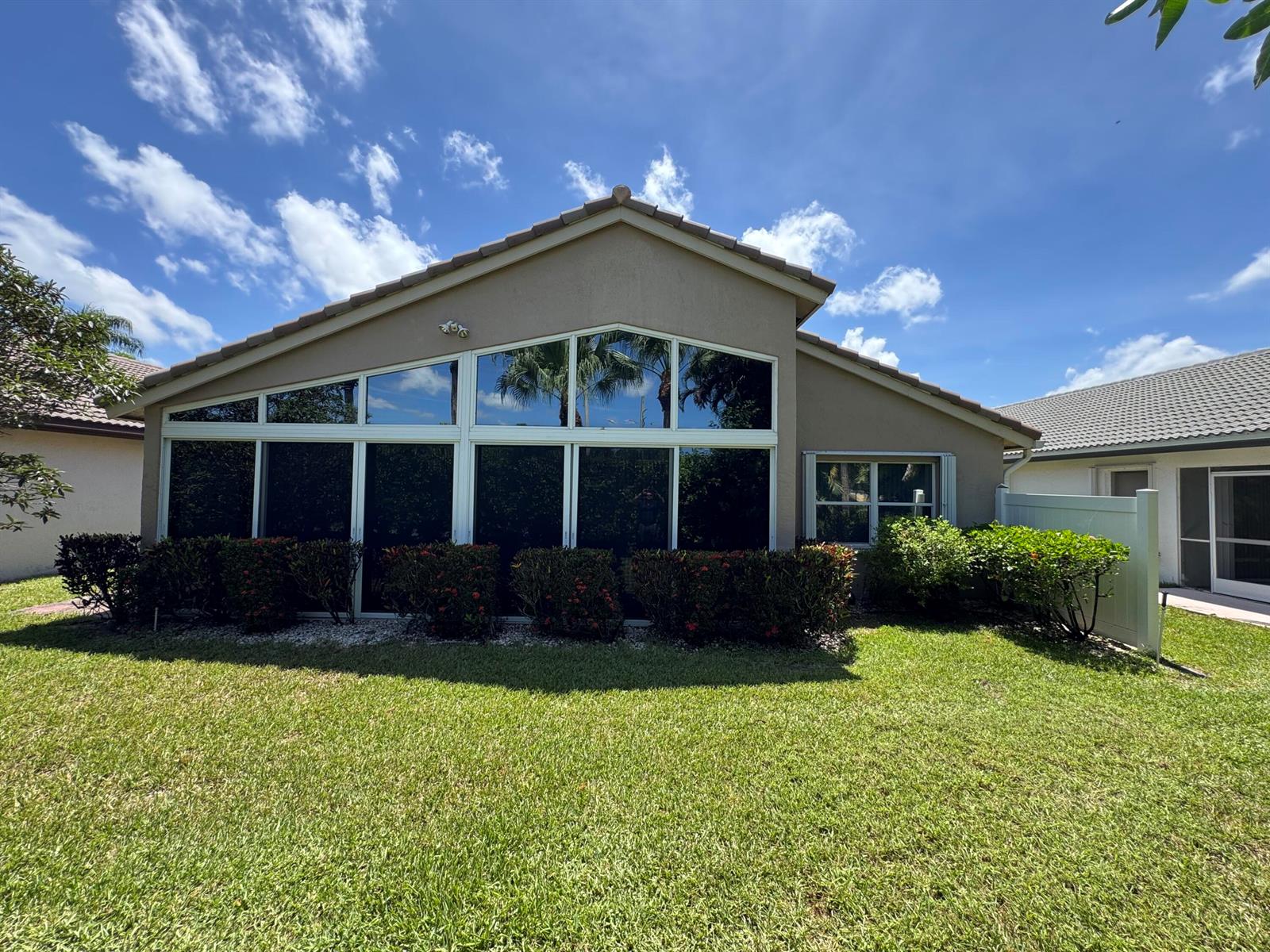 The exterior of a tan house features a large wall of windows and a manicured lawn — 6693 Sun River Road, Boynton Beach FL 33437, BOYNTON BEACH, FL