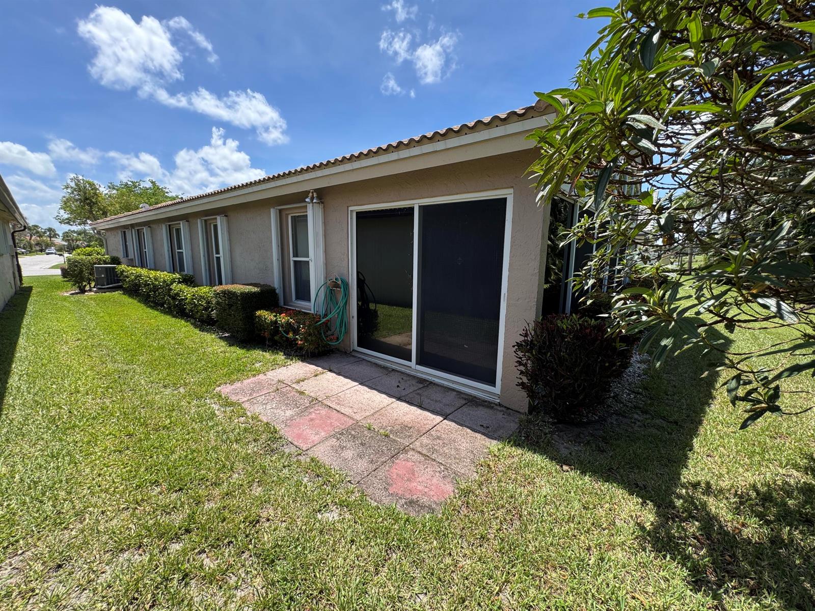An exterior view of a tan house with a sliding glass door and concrete patio — 6693 Sun River Road, Boynton Beach FL 33437, BOYNTON BEACH, FL