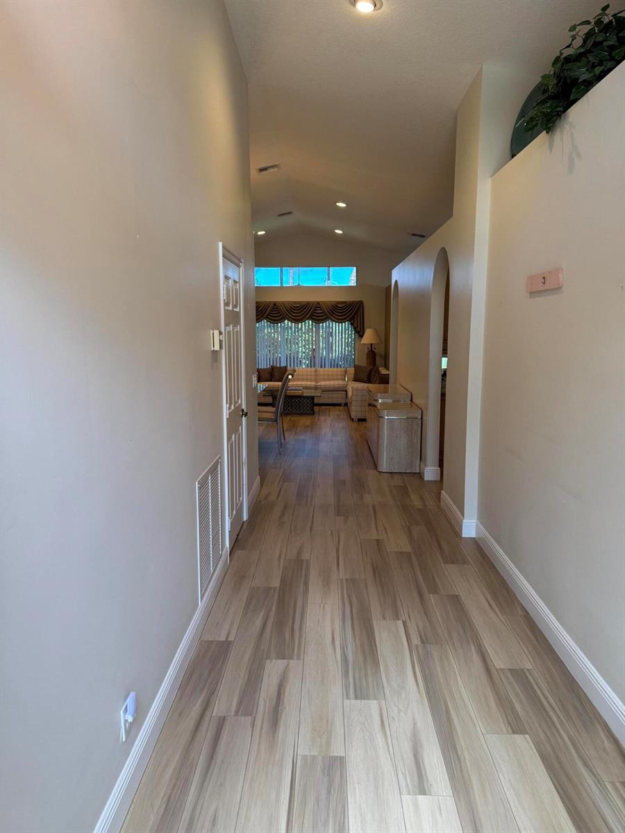 A hallway with light wood-look flooring leads toward a living area with vaulted ceilings — 6693 Sun River Road, Boynton Beach FL 33437, BOYNTON BEACH, FL