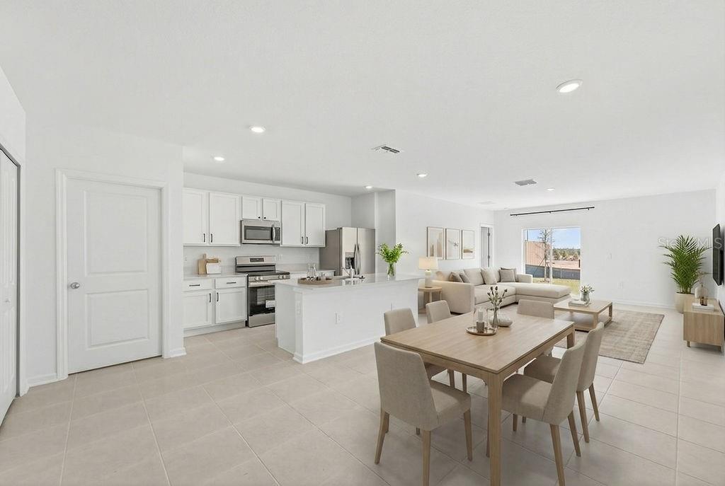 An open-concept kitchen, dining area, and living room featuring white cabinetry and light tile flooring — 1936 WILDER WAY, EAGLE LAKE, FL