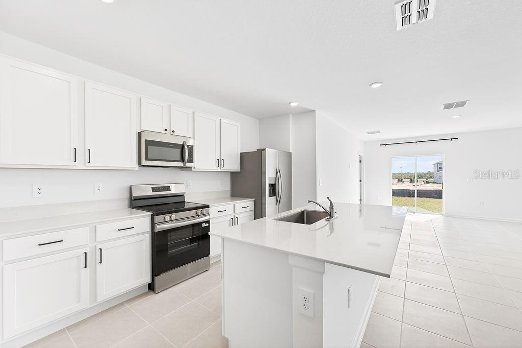 A modern kitchen features white cabinets, stainless steel appliances, and a central island with seating — 1936 WILDER WAY, EAGLE LAKE, FL