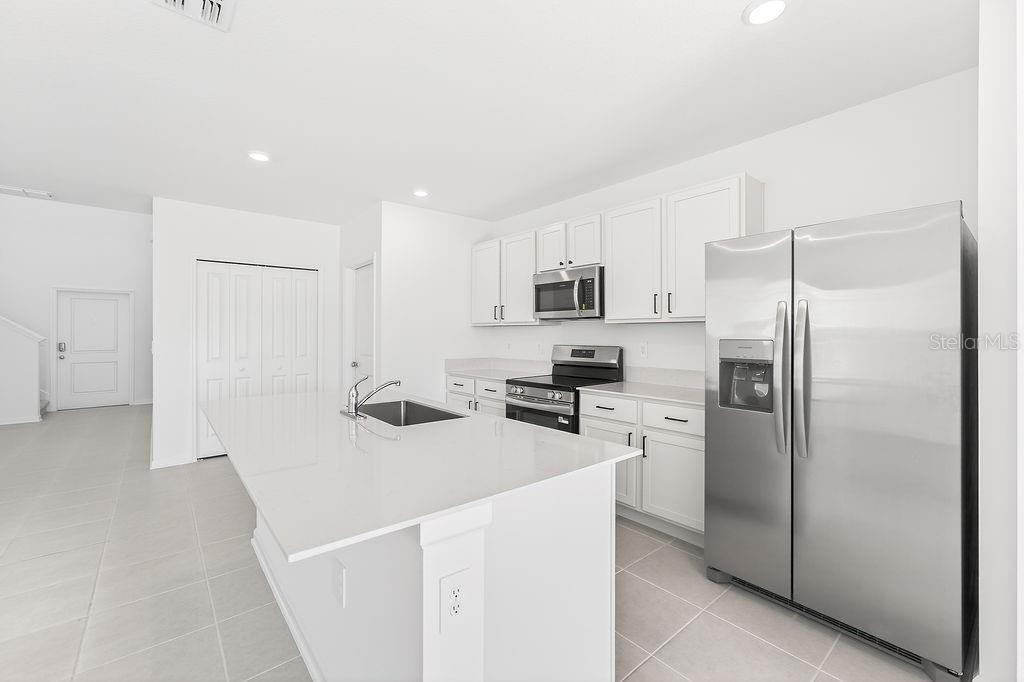 A modern kitchen features white cabinets, stainless steel appliances, and a large central island — 1936 WILDER WAY, EAGLE LAKE, FL