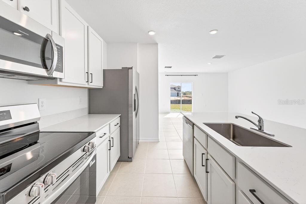 A modern kitchen features white cabinets, stainless steel appliances, and a central island with sink — 1936 WILDER WAY, EAGLE LAKE, FL