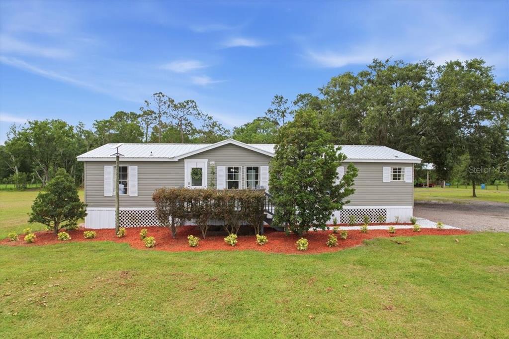 A single-story manufactured home with gray siding and a white metal roof sits on grass — 4450 QUAIL ROOST RD, ST CLOUD, FL
