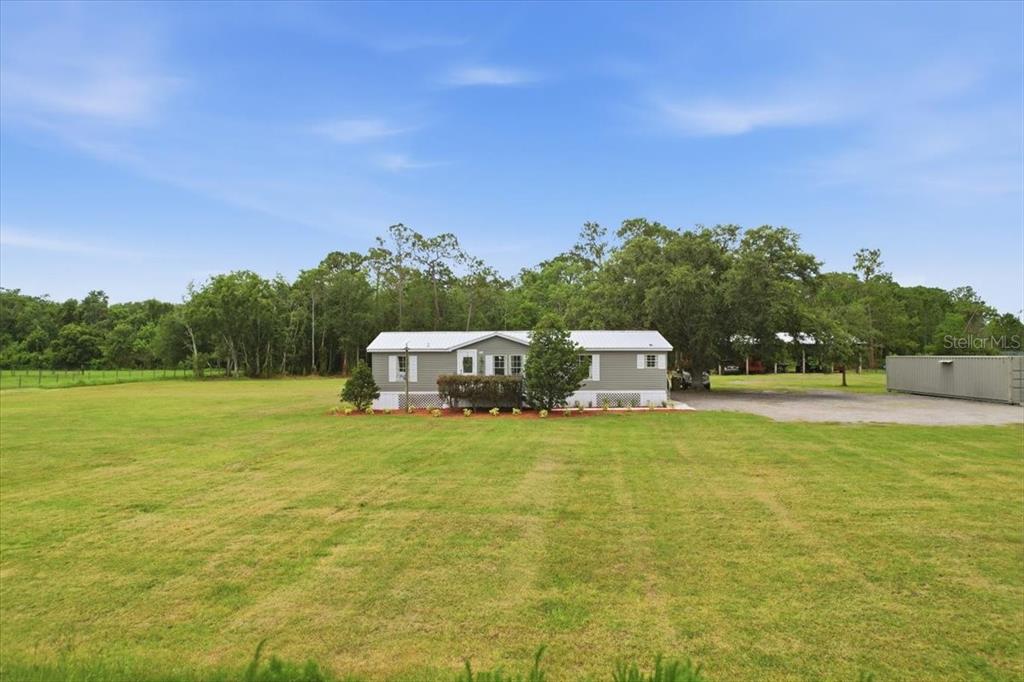 A single-story manufactured home sits on a large, grassy lot with surrounding trees — 4450 QUAIL ROOST RD, ST CLOUD, FL