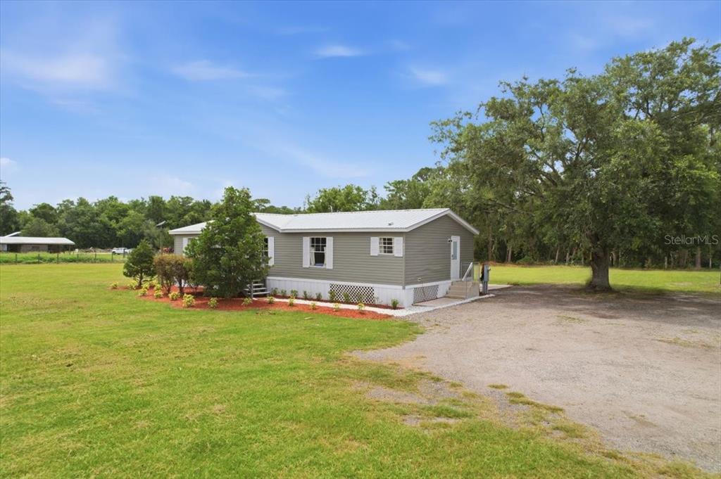 A single-story manufactured home with gray siding sits on a large, grassy rural lot — 4450 QUAIL ROOST RD, ST CLOUD, FL