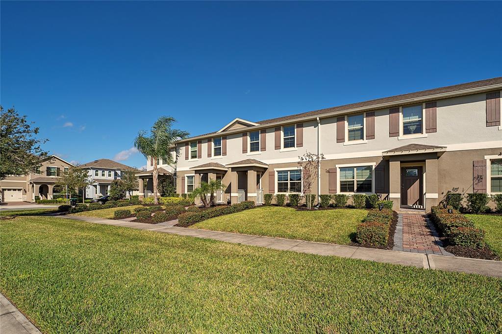 A row of two-story townhomes with beige stucco siding, brown shutters, and manicured front lawns — 16931 RESEDA ALLEY, WINTER GARDEN, FL