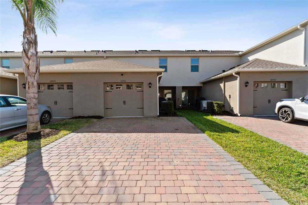 A row of townhouses features beige stucco exteriors, paved driveways, and attached garages — 16931 RESEDA ALLEY, WINTER GARDEN, FL