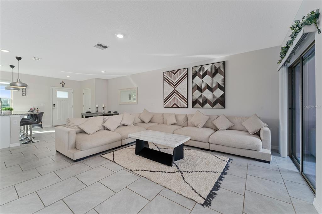 A spacious living room features a large sectional sofa, a marble coffee table, and tile flooring — 16931 RESEDA ALLEY, WINTER GARDEN, FL