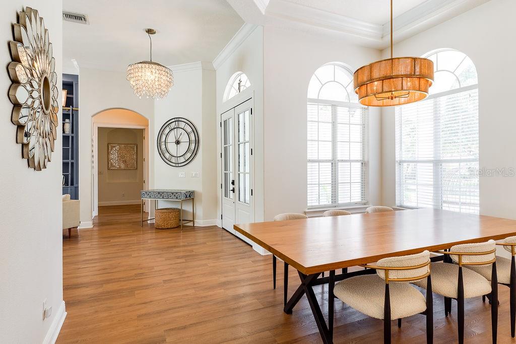 A dining room features a wooden table, modern chairs, two chandeliers, and large arched windows — 11027 HAWKSHEAD COURT, WINDERMERE, FL