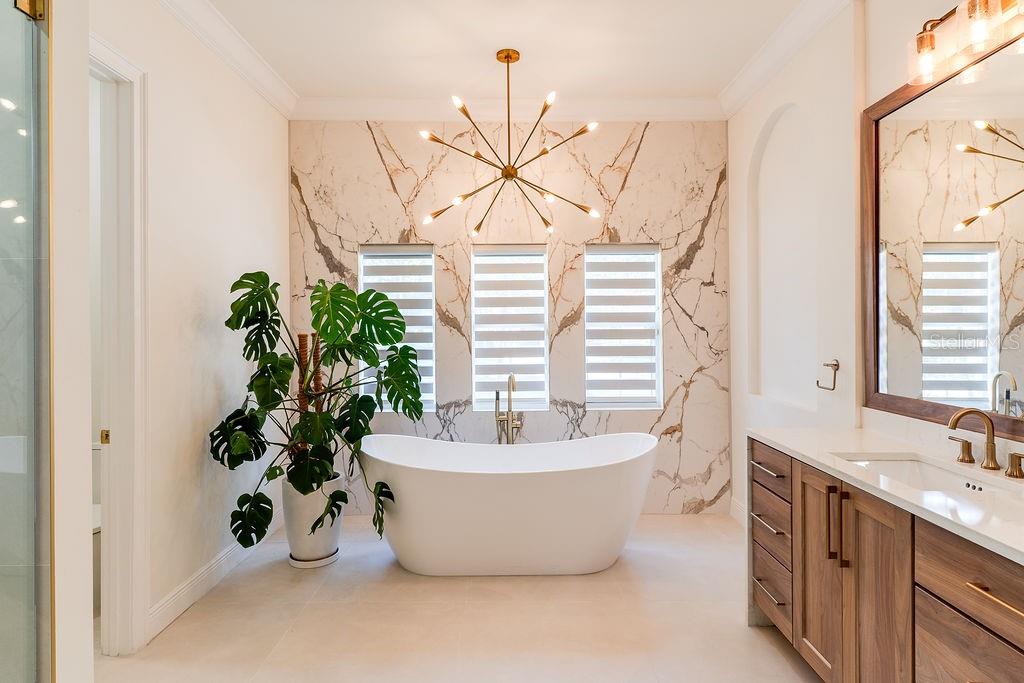 A modern bathroom features a freestanding tub, marble accent wall, and a sputnik chandelier — 11027 HAWKSHEAD COURT, WINDERMERE, FL