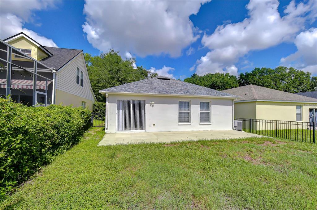 The backyard features a concrete patio, a white stucco house, and a black metal fence — 6010 SKYLARKCREST DRIVE, LITHIA, FL