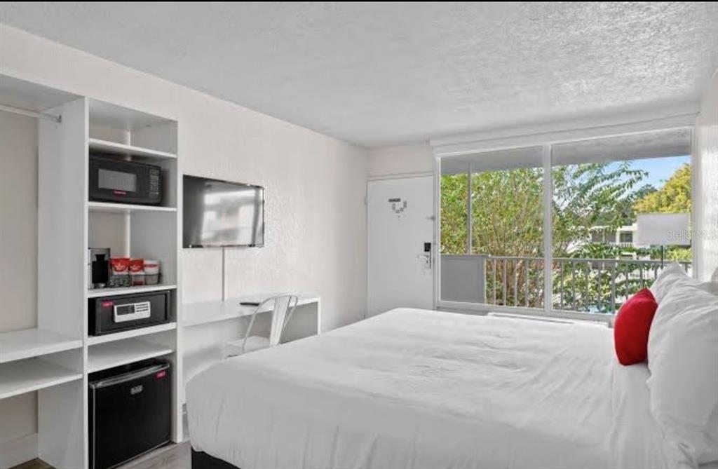 A hotel room features a bed, a desk, a shelving unit with appliances, and a balcony — 2930 NE POLYNESIAN ISLE UNIT 219, KISSIMMEE, FL