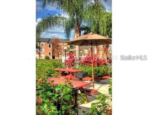 An outdoor patio area features picnic tables under a large umbrella surrounded by tropical landscaping — 5713 GATLIN AVENUE UNIT 211, ORLANDO, FL