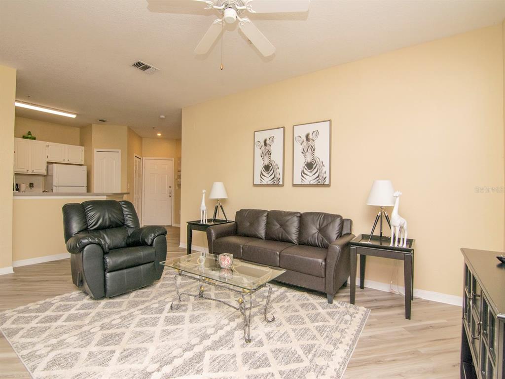 A living room features a leather sofa, a recliner, a glass coffee table, and zebra art — 5815 LEGACY CRESCENT PLACE UNIT 202, RIVERVIEW, FL
