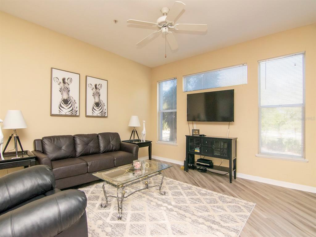 A living room features a dark leather sofa, a glass coffee table, and a television — 5815 LEGACY CRESCENT PLACE UNIT 202, RIVERVIEW, FL
