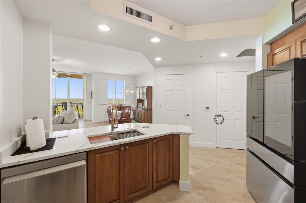 A kitchen with wood cabinets and white countertops overlooks a dining area and balcony — 3191 MATECUMBE KEY ROAD UNIT 701, PUNTA GORDA, FL