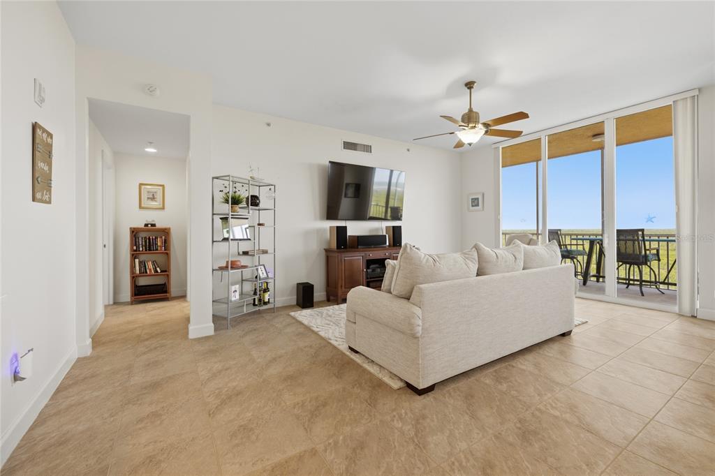 A living room features a beige sofa, a television, a metal shelf, and balcony access — 3191 MATECUMBE KEY ROAD UNIT 701, PUNTA GORDA, FL