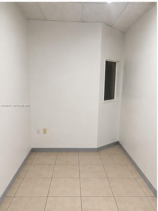 An empty office room with white walls, beige tile flooring, and a small rectangular window — 5555 NW 74th Ave # 5555, Miami FL 33166, MIAMI, FL