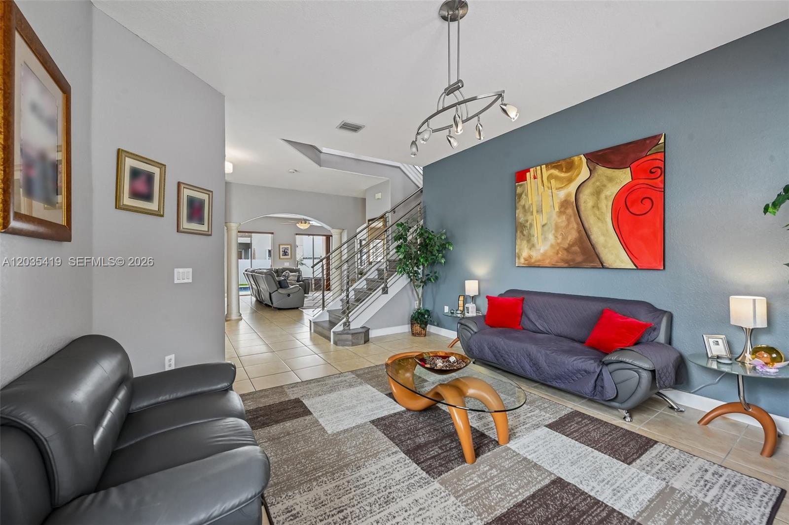 A living room features a gray sofa, a glass coffee table, and a staircase — 18159 NW 90th Ave, Hialeah FL 33018, HIALEAH, FL