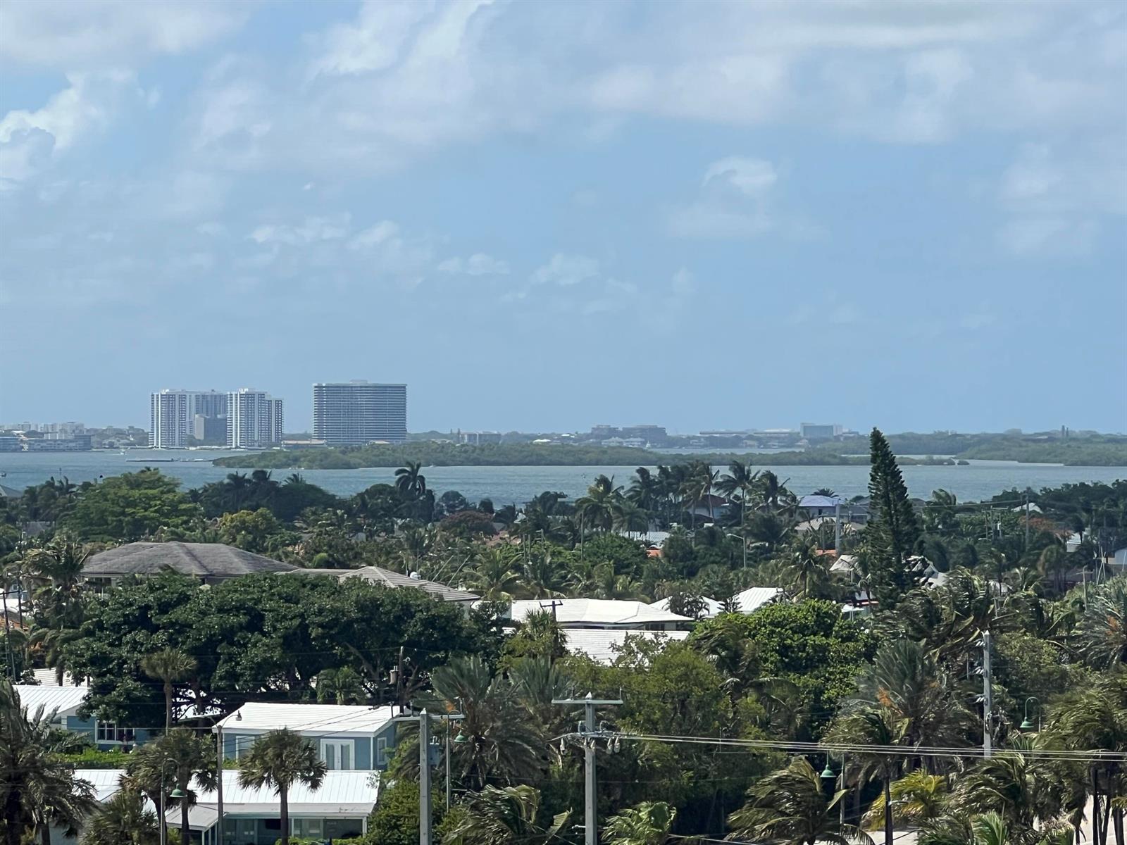 An elevated view of a coastal neighborhood with palm trees, houses, and distant high-rise buildings — 3400 N Ocean Drive # 803, Riviera Beach FL 33404, RIVIERA BEACH, FL