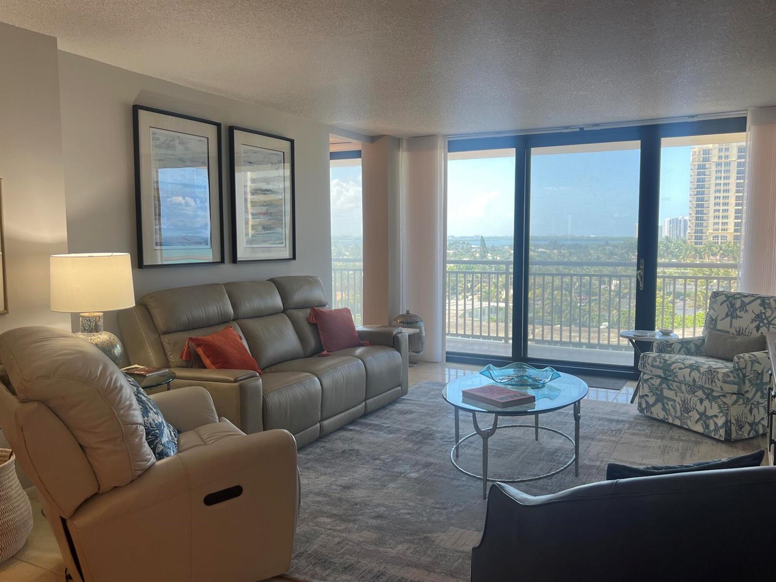 A living room features a leather sofa, patterned armchair, glass coffee table, and floor-to-ceiling windows — 3400 N Ocean Drive # 803, Riviera Beach FL 33404, RIVIERA BEACH, FL