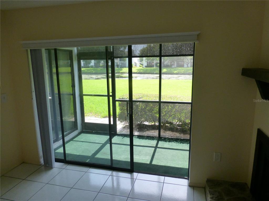 A tiled room features sliding glass doors opening to a screened-in patio overlooking a lawn — 119 LAKESIDE DRIVE UNIT 119, OLDSMAR, FL