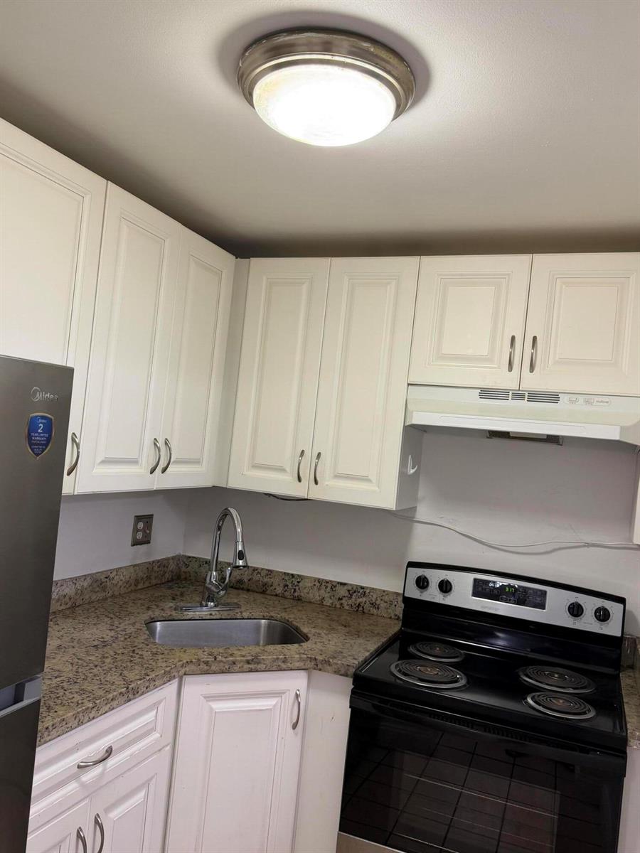 A kitchen features white cabinets, granite countertops, a stainless steel sink, and a black stove — 270 S Cypress Road # 204, Pompano Beach FL 33060, POMPANO BEACH, FL