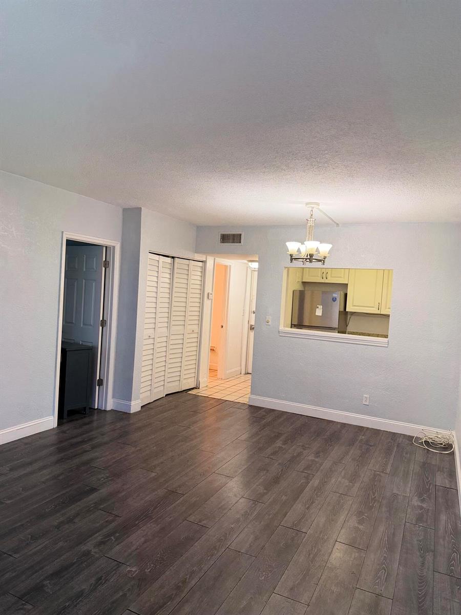 A living room with gray wood-look flooring, a pass-through window to the kitchen, and closets — 270 S Cypress Road # 204, Pompano Beach FL 33060, POMPANO BEACH, FL