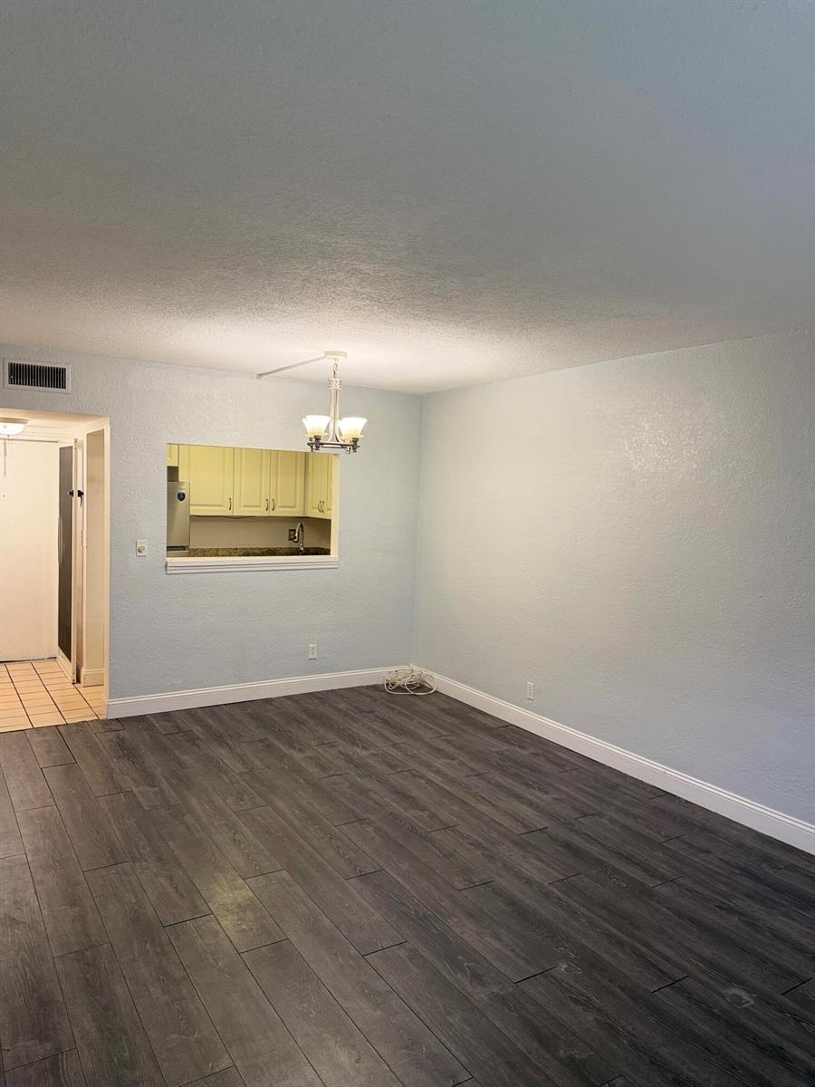 An empty room with light blue walls, dark wood-look flooring, and a kitchen pass-through window — 270 S Cypress Road # 204, Pompano Beach FL 33060, POMPANO BEACH, FL