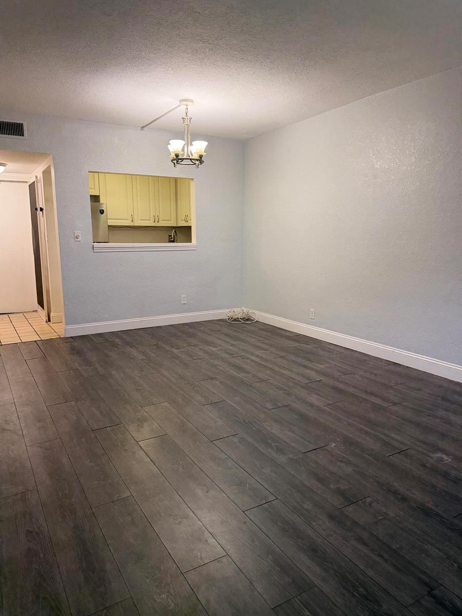 An empty room with light blue walls, dark wood-look flooring, and a kitchen pass-through window — 270 S Cypress Road # 204, Pompano Beach FL 33060, POMPANO BEACH, FL