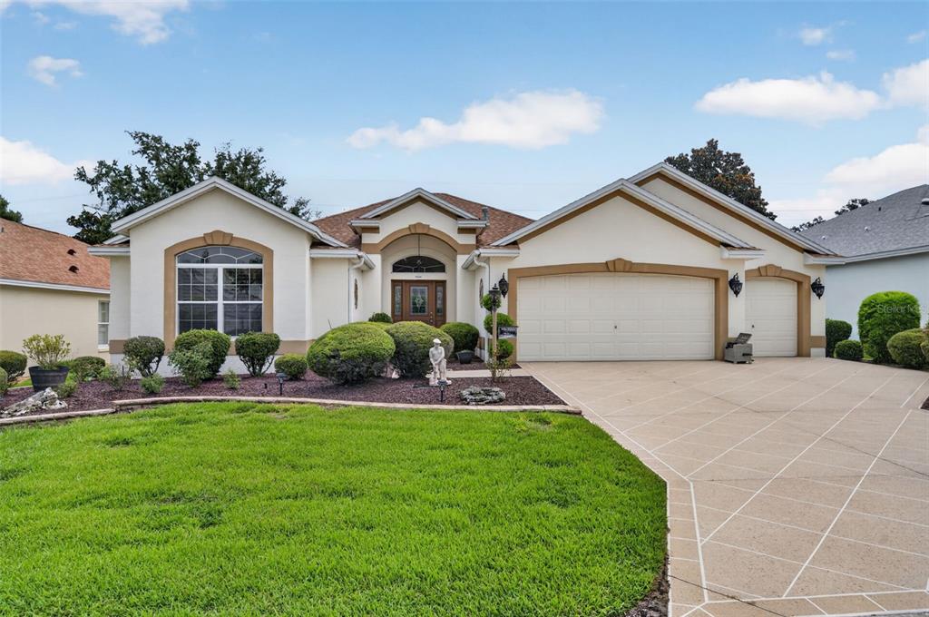 A single-story suburban house with a tan stucco exterior, a three-car garage, and landscaping — 17246 SE 85TH WILLOWICK CIRCLE, THE VILLAGES, FL