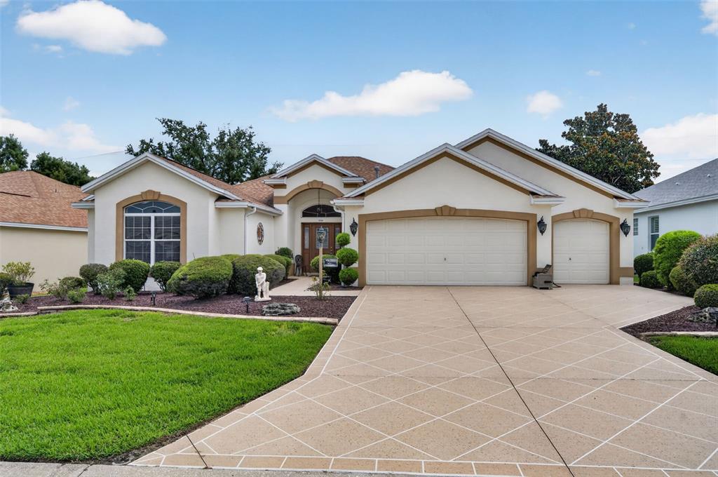 A single-story house with a beige stucco exterior, a patterned driveway, and a three-car garage — 17246 SE 85TH WILLOWICK CIRCLE, THE VILLAGES, FL